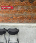 Official Kansas City Chiefs NFL Aluminum Metal Street Sign 4X15 Inch mounted on a rustic brick wall above black bar stools.