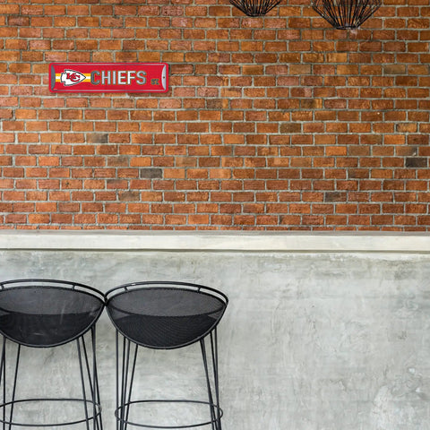 Official Kansas City Chiefs NFL Aluminum Metal Street Sign 4X15 Inch mounted on a rustic brick wall above black bar stools.