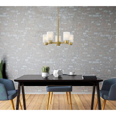 Five Light Indoor Chandelier In Champagne Brass Finish With Frosted Glass, hanging over a dining table against a brick wall.