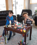 Children using Premium Natural Wood Craft Sticks For DIY Arts And Crafts at a table full of craft supplies in a living room.