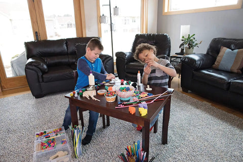 Children using Premium Natural Wood Craft Sticks For DIY Arts And Crafts at a table full of craft supplies in a living room.