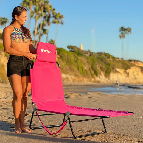 Woman setting up pink 2-leg chaise lounge chair with polyester comfort, reclining back, headrest pillow on beach