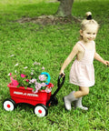 Child pulling a red push and pull walker wagon with garden tools and flowers, suitable for kids aged one to four years old.