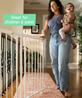 Woman holding baby next to Stairway 46W Series Baby Gate for Stairs and Dog Gate Indoor With Door, white metal safety gate in hallway.