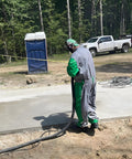 Worker wearing Kick Grit To The Curb With This Badass Green Blast Suit Spray Paint Protective Coveralls using a hose on a job site.