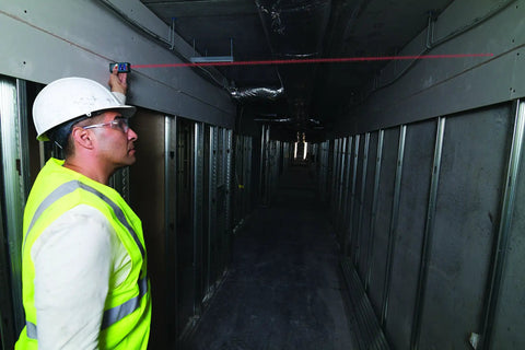 GLM 50 C Laser Distance Meter 165 Ft With Backlit Display used by construction worker in hallway for measurements