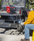 Welder wearing Auto Darkening Welding Helmet With Grind Mode 7-13 Shade, working outdoors, welding ATV trailer.