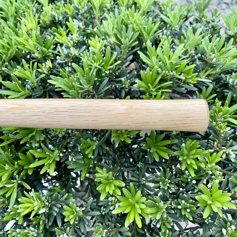 Oak handle of 14 Inch Tough As Nails Narrow Hoe Japanese Carbon Steel Garden Tool for digging, shown against green foliage.