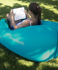 Person sitting on Inflatable Lounger Air Chair Lightweight Self Inflating Beach Chair with book in teal color outdoors