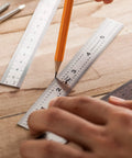 Close-up of Pro Grade Machinist Ruler Set, 6 Inch Stainless Steel with precise markings being used for drafting on wood surface.