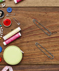 Big Heavy Duty Black Safety Pins Pack Of 50 For Scarves Hats And Crafts With Super Strong Lock and Super Smooth Opening You Will Love These Badboys For Any Industrial Or Outdoor Job Today on wooden surface with thread and buttons.
