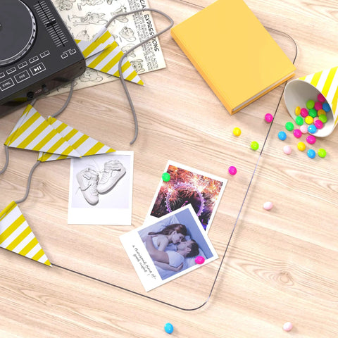 Wooden desk surface with scattered yellow books, colorful party decorations, and printed photographs.
