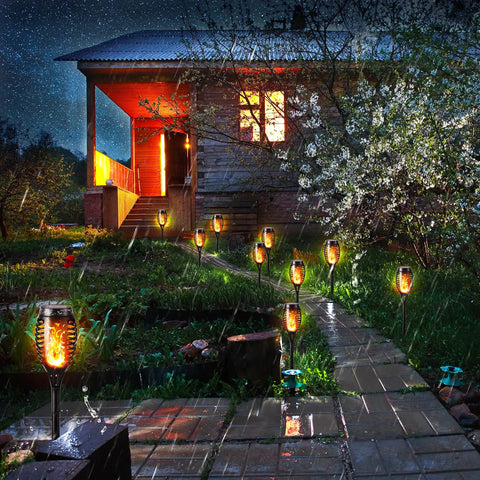 12 Pack Solar Torch Lights With Flickering Flames For Outdoor Use illuminating a garden pathway beside a house at night