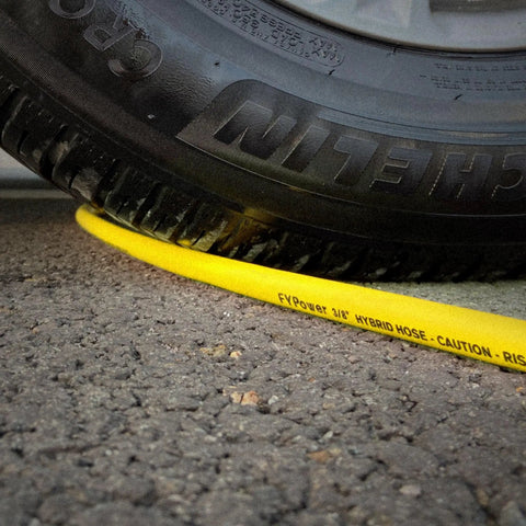 Heavy Duty Hybrid Air Compressor Hose 3/8 Inch X 50 Foot Lightweight Kink Free Airline under a tire on asphalt.