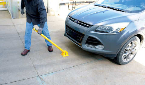 Person using Tough As Nails Ground Mount Heavy Duty Steel Fold Down Bollard to secure driveway near parked car.