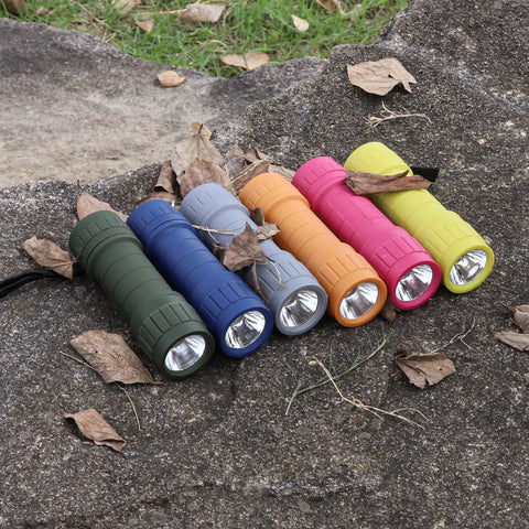 Six Pack Of Compact LED Flashlights With 100 Lumen Output Includes 18 AAA Batteries Mini Pocket Lights For Camping Hiking Emergencies Outdoor Adventure Kit displayed on rock