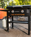 28 Inch Griddle With Protective Hood And Counter Height Side Shelves In Powder Coated Steel For Outdoor Grilling, 524 Square Inches Of Cooking Space, Perfect For Feeding A Crowd shown in camping setting