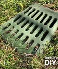 Green ground-level grate for downspout and sump pump discharge extension, fits 3 or 4 inch pipe, in lawn setting