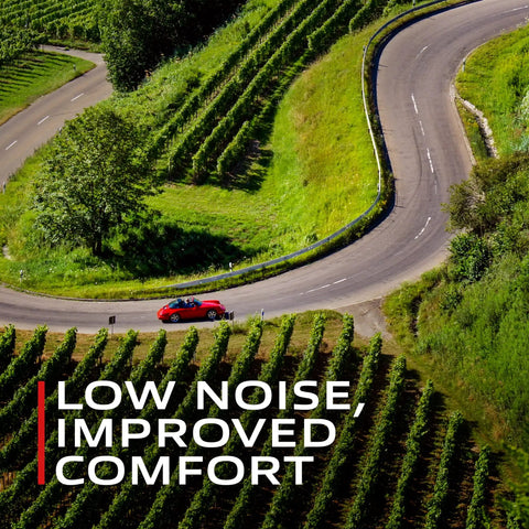 A red car on a winding road with green hills, showcasing low noise and improved comfort from Premium Ceramic Front Disc Brake Pad Set.