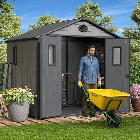 Man with wheelbarrow in front of 8x6 Ft Resin Storage Shed With Floor For Backyard And Outdoors, Built To Last Durable Plastic Tool Shed