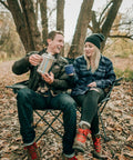 Couple enjoying coffee with Camper's Percolator Coffee Pot For Camping 9 Cup Aluminum in a forest setting.