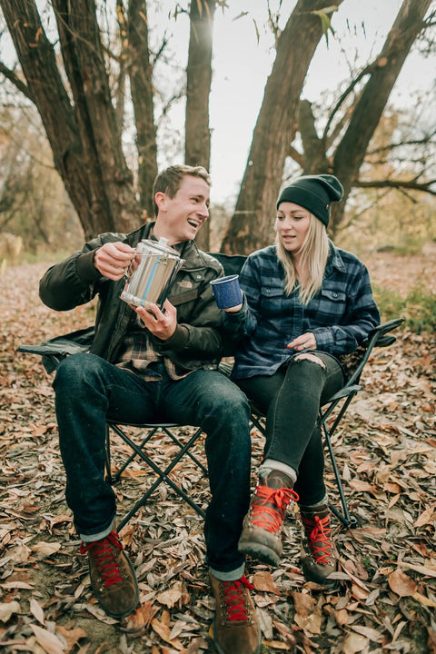 Couple enjoying coffee with Camper's Percolator Coffee Pot For Camping 9 Cup Aluminum in a forest setting.