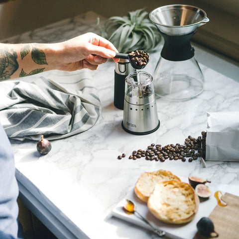 Portable Electric Coffee Grinder With Stainless Steel Burrs And Nine Precision Settings For Espresso To French Press Compact Grab And Go Design With No Sweat Cleanup For Top Shelf Daily Grinds Anywhere, person adding beans.