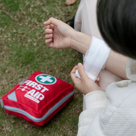 General Medi red reflective first aid kit bag, small compact 175-piece kit, person wrapping a bandage outdoors.