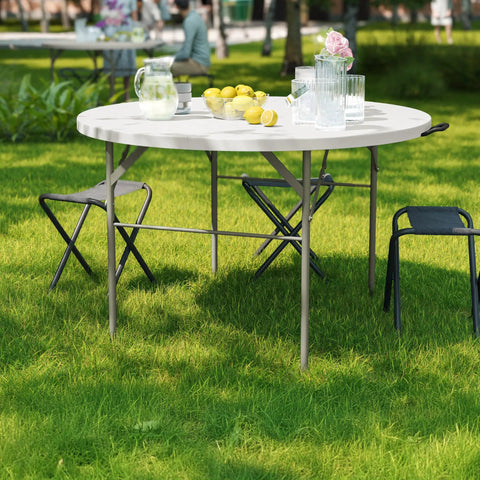 Grab And Go Ready 4 Foot Round Folding Plastic Table With Carrying Handle For Indoor And Outdoor Events Portable And Lightweight Party Surface That Seats Up To Four People White in a garden setting.
