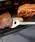 Side view of Cuisinart stainless steel grill spatula flipping two large beef roasts on a barbecue grill