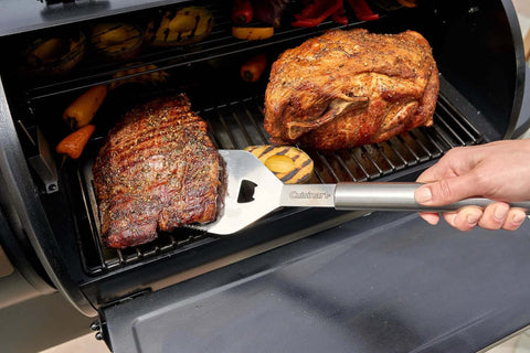 Side view of Cuisinart stainless steel grill spatula flipping two large beef roasts on a barbecue grill