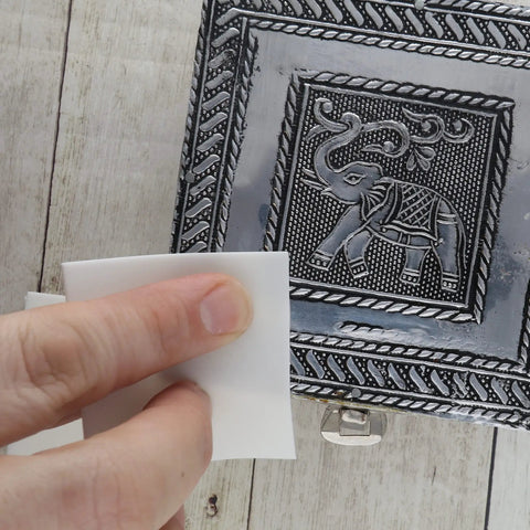 Using Shine Rite 2-Inch Polishing Pads For Jewelry to polish a metal box with an elephant design.
