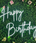Lit Two Line Happy Birthday Neon Sign LED Light For Party Backdrop And Photo Booth Vibes against greenery wall with roses