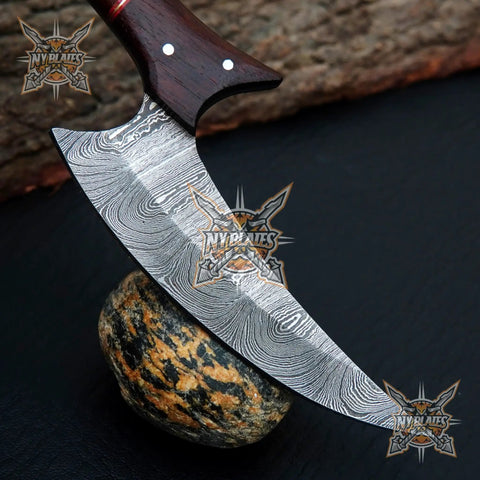 Beast Damascus Steel Skinner Knife with wood handle and leather sheath on rock