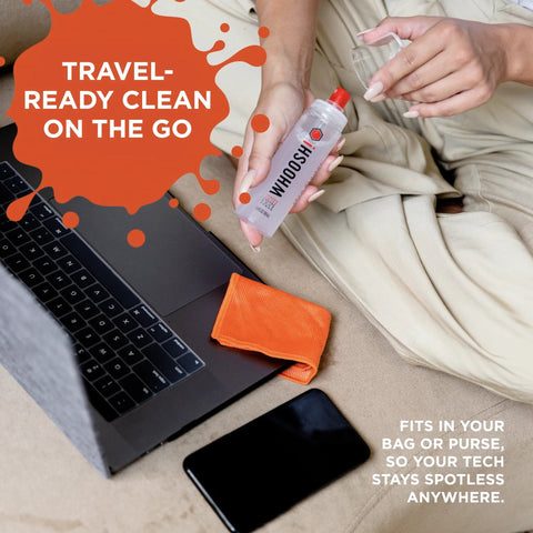 WHOOSH! Screen Shine Duo XL spray bottle with red cap and orange microfiber cloth beside laptop and smartphone.