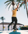 Skater using Stimulus 70mm 86A Freeride Longboard Wheels Yellow Set of 4 to perform freestyle tricks under palm trees