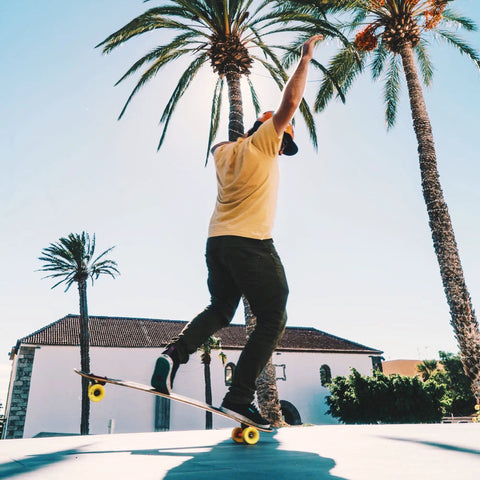 Skater using Stimulus 70mm 86A Freeride Longboard Wheels Yellow Set of 4 to perform freestyle tricks under palm trees