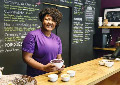 Person holding a bowl at a cafe counter with a chalkboard menu in the background