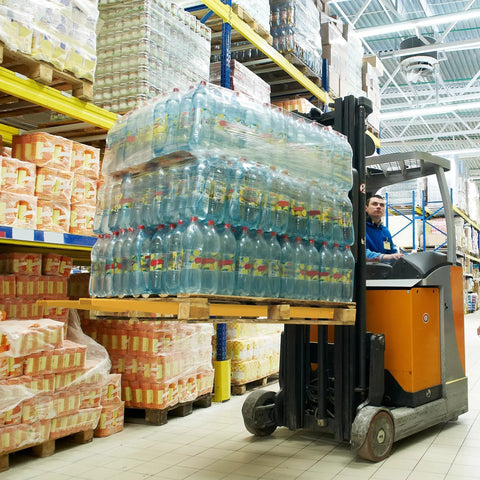 Forklift with orange body lifting a pallet of plastic bottled water in a warehouse