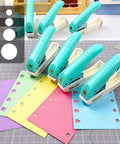 Sky blue one-handed 2mm circle pattern embosser with built-in waste storage, shown on a crafting table with colorful paper and shapes.
