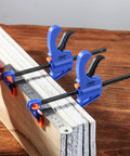 Woodworking Bar Clamps 4 Inch Set of 2 Quick Release One Handed Clamps With Hardened Steel Bar And Soft PVC Pads For Small DIY Projects 65 Lb Clamping Force Blue, clamping wooden boards on a table.