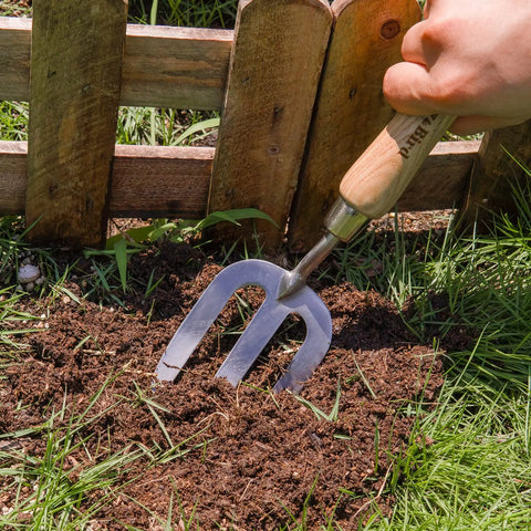 Person using Stainless Steel Hand Fork For Weeding And Planting, Traditional Garden Tool With Ergonomic Ash Wood Handle in soil