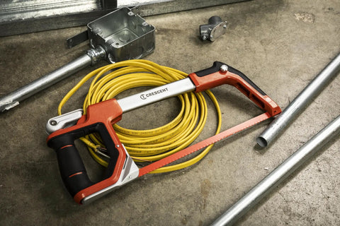 12 Inch Fast Tension Hacksaw With Dual Material Handle, On Board Blade Storage, and metal pipes in a workshop setting