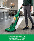 Heavy Duty Bagless Upright Vacuum Chomping Debris On Carpets Hardwood Floors And Furniture With Beastly Suction Plus Onboard Tools and Commercial Filtering For Daily Grind Cleaning in use on tiled flooring.