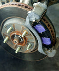Automotive brake rotor and caliper assembly; rusted hub, purple brake pads visible
