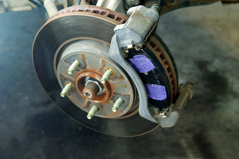 Automotive brake rotor and caliper assembly; rusted hub, purple brake pads visible