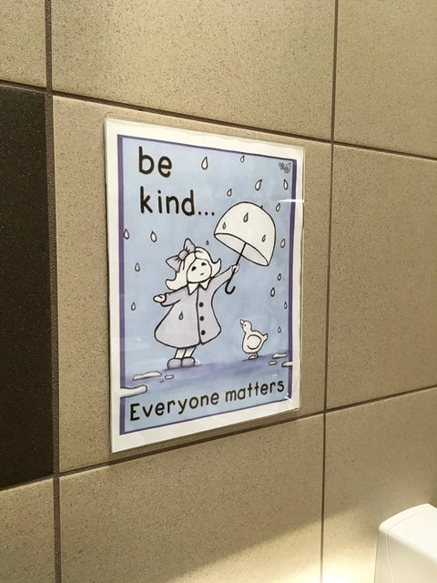 8.5x11 Clear Acrylic Sign Holders With No Drilling Mount, holding 'Be Kind' poster in restroom setting, wall mounted.