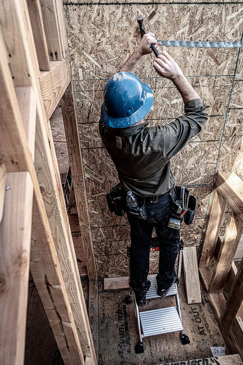 Worker on Jumbo Step Aluminum 2 Step Stool Ladder, Lightweight Yet Sturdy With A 375 Pound Duty Rating, hammering wall.
