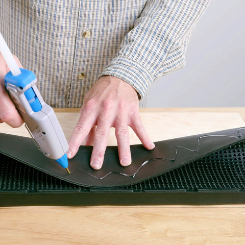 Person using Full Size Hot Glue Gun Kit With 3 Nozzles, 75 Watt Heater, Ergonomic Grip, applying glue to a black surface.