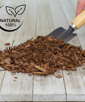 Pile of organic orchid potting bark on wooden surface with a trowel, "One Hundred Percent Organic Orchid Potting Bark Eight Quarts All Natural Pine Bark Mix Additive For Orchids And Epiphytes With Dope Drainage And Airy Roots For Indoor And Outdoor Container Gardening" label visible.